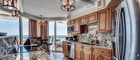 A modern kitchen with granite countertops, wooden cabinets, stainless steel appliances, and a view of the ocean.