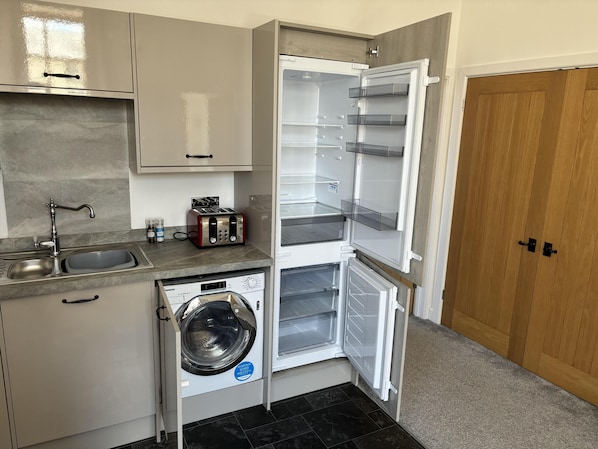 Una cocina compacta con lavadora integrada, tostadora y lavabo.