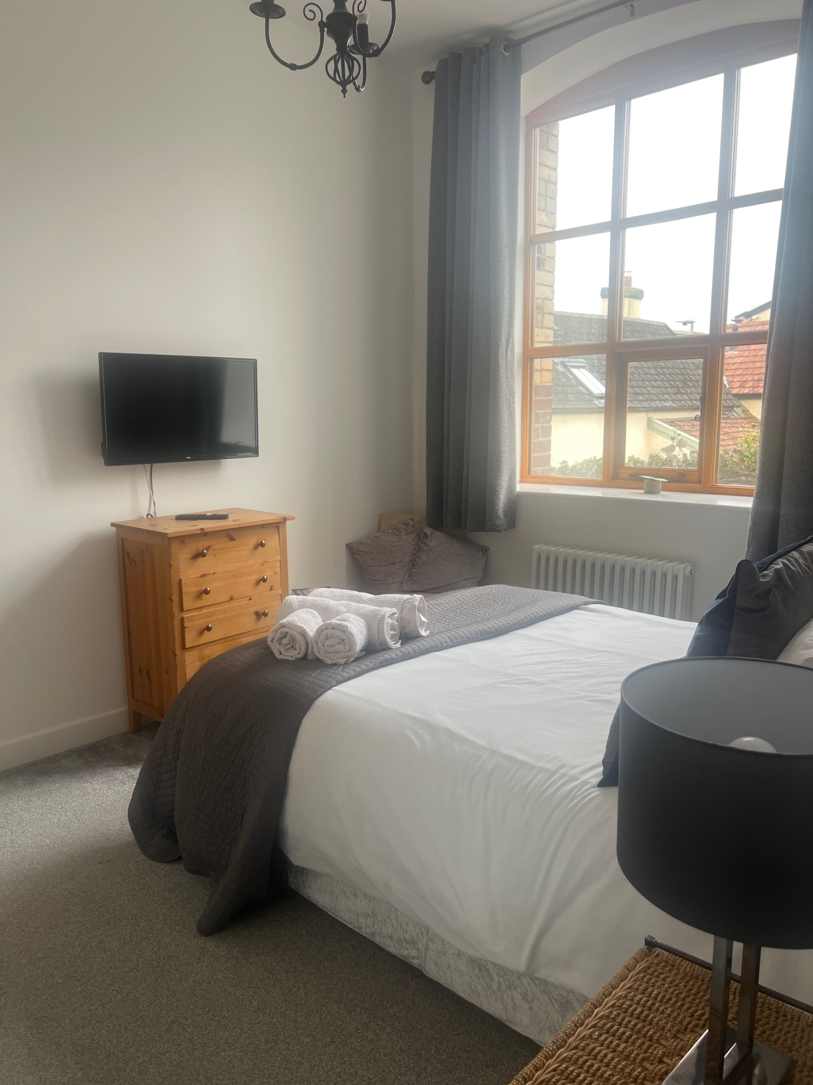 A bedroom with a bed, a TV, a dresser, and a window with curtains.