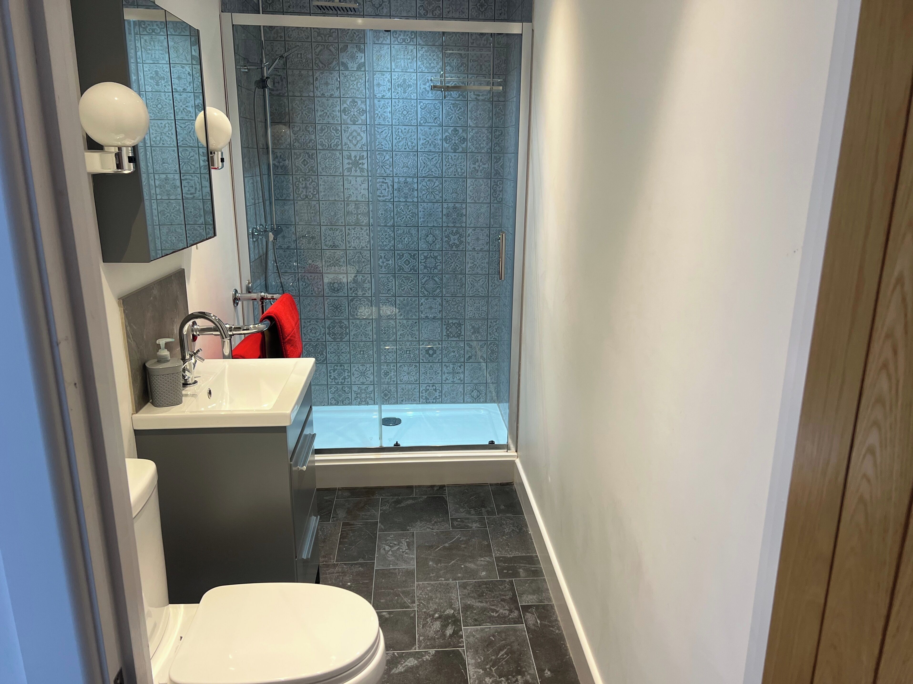 Un baño pequeño con un lavabo blanco, un inodoro y una zona de ducha con azulejos de diseño azulado.
