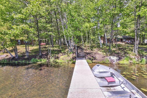 A wooden dock leading to a small boat, surrounded by a forested area with a cabin and a swing. - Estrold's Resort-Maple Cabin (St.Germain)