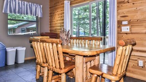 A wooden dining table with chairs, a window with curtains, and a view of trees outside. - Estrold's Resort-Maple Cabin (St.Germain)