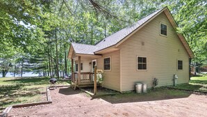 A small, single-story cabin with a porch, situated in a wooded area near a body of water. - Estrold's Resort-Maple Cabin (St.Germain)