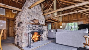 Un acogedor interior de cabaña con chimenea de piedra, vigas de madera y un espacio de estar confortable.