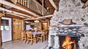 Interior rústico de una cabaña con chimenea de piedra, mesa de comedor de madera y sillas.