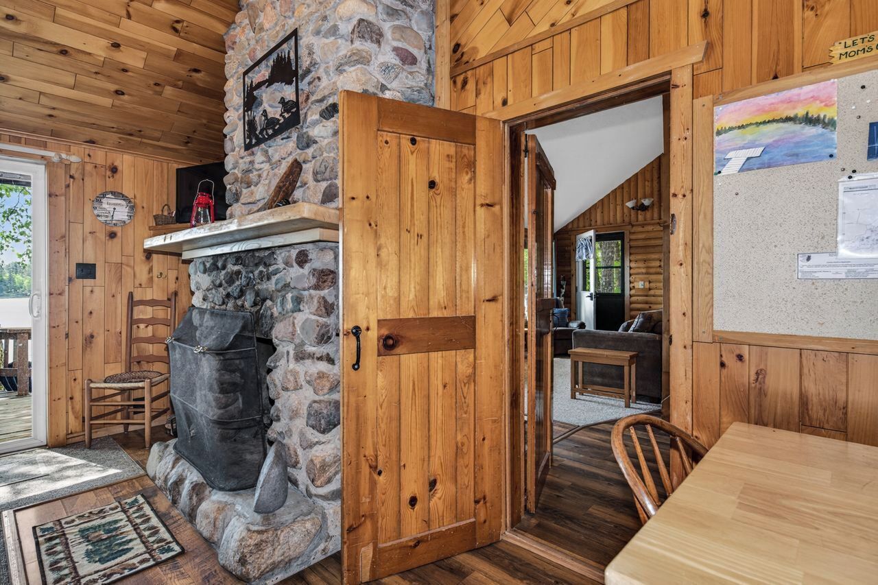 Ein rustikales Blockhaus-Interieur mit Kamin aus Stein, Holzwänden, einem Essbereich und einem gemütlichen Wohnraum.