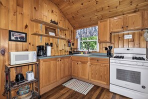 Une cuisine rustique, située dans une cabane en bois, équipée d’un four à micro-ondes, d’un grille-pain, d’une cuisinière et de meubles de rangement en bois.