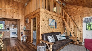 Interior de una cabaña de madera con cocina, comedor, sala de estar con sofá y una escalera.