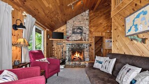 Interior acogedor de una cabaña con chimenea de piedra, paredes de madera, televisión y un mapa en la pared.