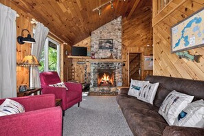 L’intérieur d’un chalet accueillant, avec une cheminée en pierre, des murs en bois, un téléviseur et une carte accrochée au mur.