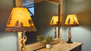 A wooden dresser with two lamps featuring tree designs, a mirror, and a small potted plant.