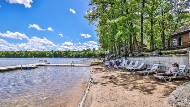 A lakeside setting with a dock, lounge chairs, and a small building.