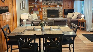 A wooden interior with a fireplace, a dining table with chairs, a sofa, and a television.