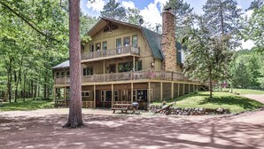 A two-story log cabin with a balcony, surrounded by trees.
