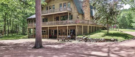 A two-story log cabin with a balcony, surrounded by trees.