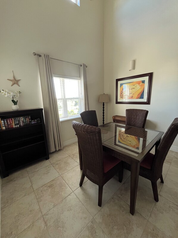 En matplats med ett bord med glasskiva, stolar i rotting, en bokhylla, en dekoration i form av en sjöstjärna och en inramad tavla på väggen.