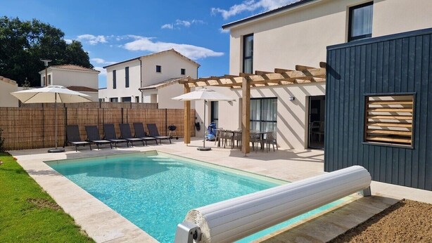 A swimming pool with lounge chairs, a pergola, and a modern building with a wooden window. - Villa 11 by Avecoeur (Saint-Augustin)
