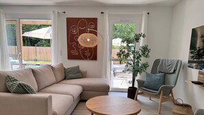 A modern living room with a beige sectional sofa, a round wooden coffee table, a grey armchair, and a large potted plant. - Villa 11 by Avecoeur (Saint-Augustin)