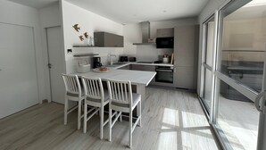 A modern kitchen with a dining area, featuring a large island, white chairs, and a view through a glass door. - Villa 11 by Avecoeur (Saint-Augustin)