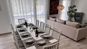 A dining area with a long table set for six, white chairs, a sofa, and a potted plant. - Villa 11 by Avecoeur (Saint-Augustin)
