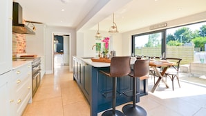 A modern kitchen with a central island, bar stools, and a view of the garden. - Adgestone Villa (Sandown)