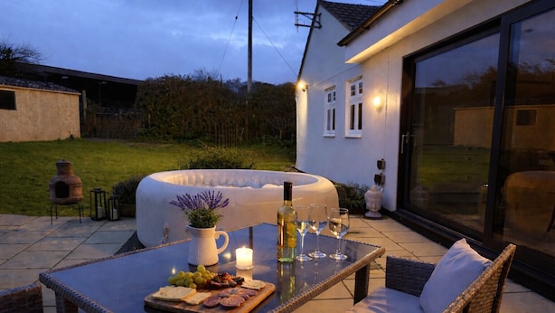 A patio with a table set for a meal, outdoor seating, a hot tub, and a house in the background. - Adgestone Villa (Sandown)