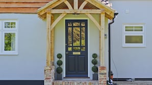 A house with a dark blue front door, a wooden porch, and brick steps. - Adgestone Villa (Sandown)