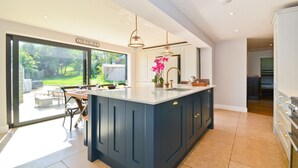 A modern kitchen with a large island, a dining area with outdoor seating, and a view of the garden. - Adgestone Villa (Sandown)