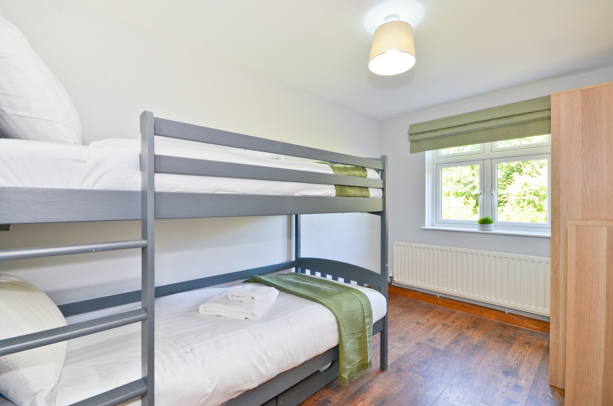 Une chambre avec un lit superposé, une fenêtre, un radiateur et une armoire en bois.