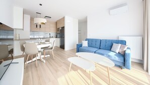 A modern living room with a blue sofa, a dining area with a white table and chairs, and a kitchen with wooden cabinets and a white countertop. - Apartamenty Sun & Snow Villa Verona (Mielno)