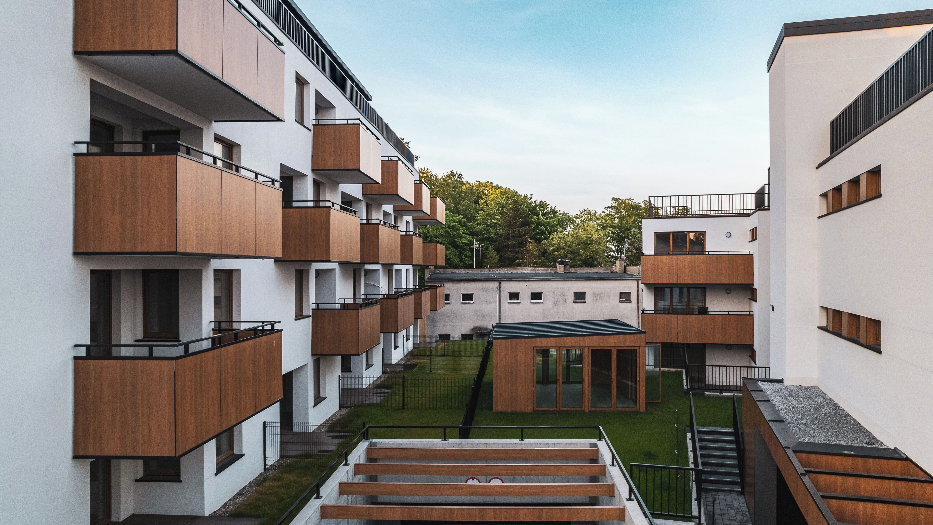 A modern apartment complex with multiple balconies, a central courtyard, and a mix of wooden and white exterior finishes.