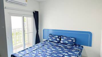 Quarto com cama, luminária no teto, ar condicionado e porta de vidro deslizante para uma varanda.
