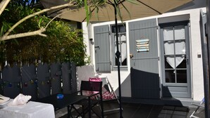 A patio area with a table and chairs, a covered seating area, and a door with a window. - Chambres D'hôte A LA Villa DU Grand Large (Biscarrosse)