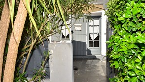 A narrow pathway leading to a white building with a grey door and windows. - Chambres D'hôte A LA Villa DU Grand Large (Biscarrosse)