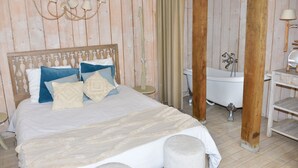 A bedroom with a wooden headboard, a bed with white and blue bedding, a nightstand, a lamp, a wooden floor, and a white bathtub. - Chambres D'hôte A LA Villa DU Grand Large (Biscarrosse)