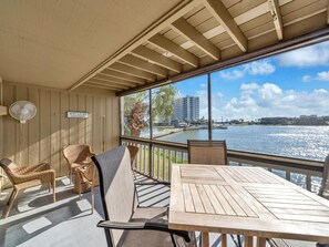 A balcony with wicker furniture, a table, and a view of a body of water with buildings in the background.