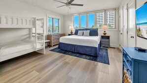 A bedroom with a bunk bed, a large bed, a ceiling fan, a TV, and a view of the beach. - Boardwalk 284- Lakefront Resort Living! Short Walk to Beach! Prime Location! (Miramar Beach)
