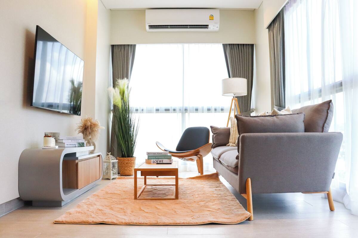 A modern living room with a flat-screen TV, a sofa, a coffee table, and a large window with curtains.