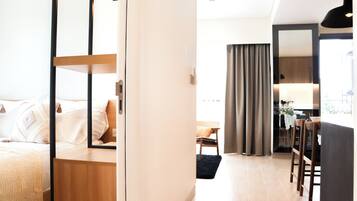A modern hotel room with a bed, a wooden nightstand, a desk, and a dining area with chairs and a table.