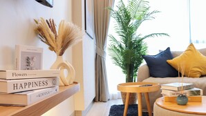A modern living room with a bookshelf, a potted plant, and a round wooden side table. - Lakeside Residences by NLA (Choeng Thale)