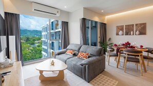 A modern living room with a grey sofa, a round coffee table, and a dining area with a small table and chairs. - Lakeside Residences by NLA (Choeng Thale)