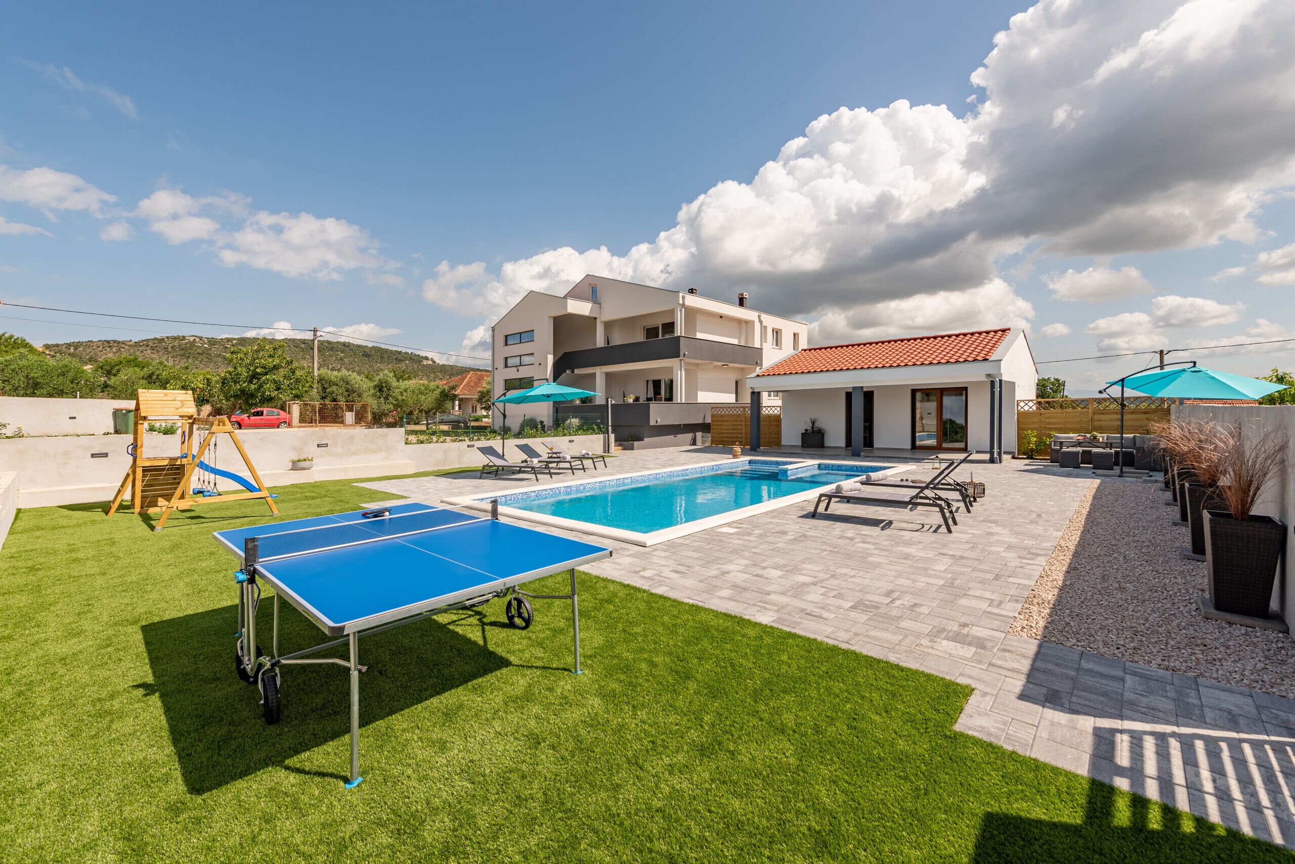 A pool area with a ping pong table, lounge chairs, and umbrellas.