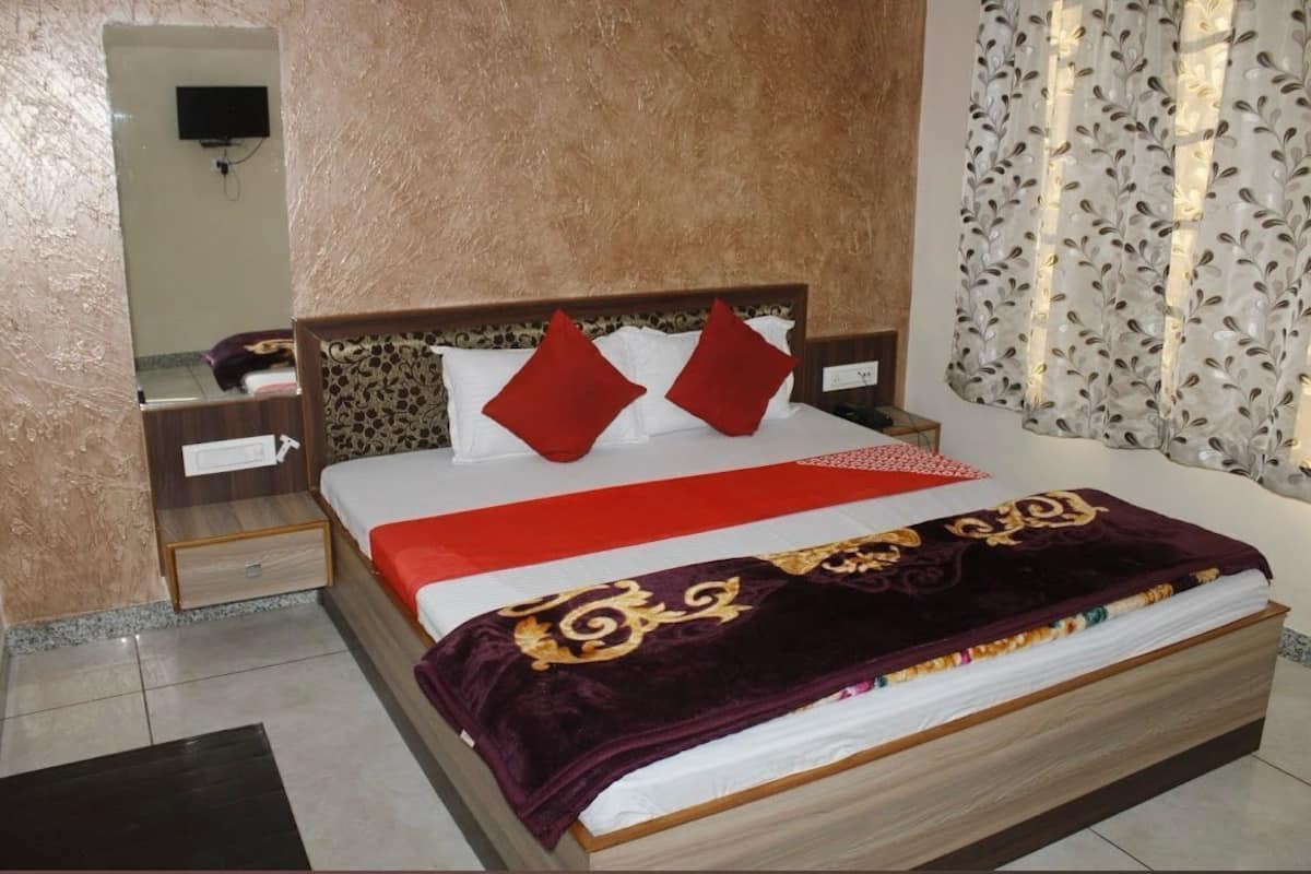 Un lit bien fait, recouvert d’une couvre-lit rouge et blanche, avec deux oreillers rouges et une couverture violet foncé ornée de motifs dorés.