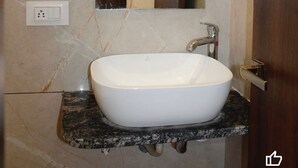 A bathroom with a white sink, a mirror, and a wooden door. - Hotel Satyam Palace (Nokha)