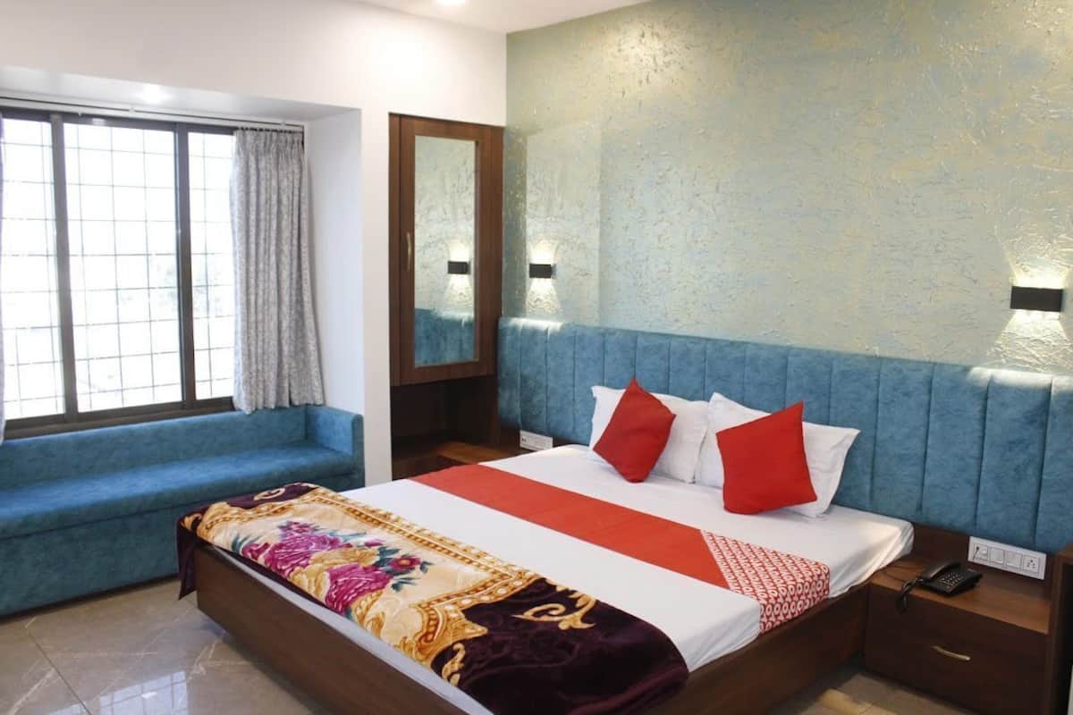 Une chambre d’hôtel avec un grand lit, un banc recouvert d’un tissu bleu, un miroir et un mur à motifs.