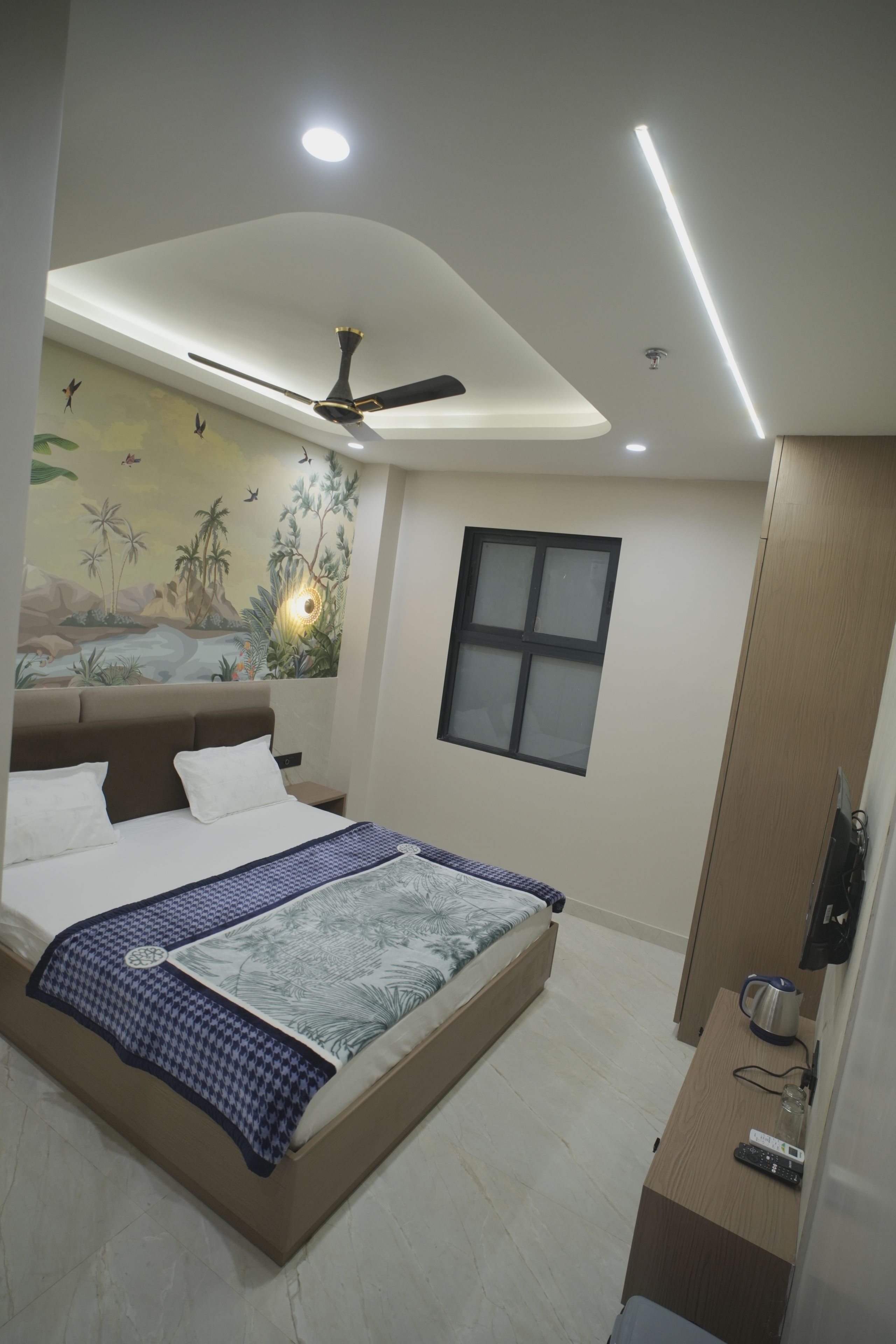 Une chambre à coucher avec un lit, un ventilateur de plafond, une fenêtre et un téléviseur fixé au mur.