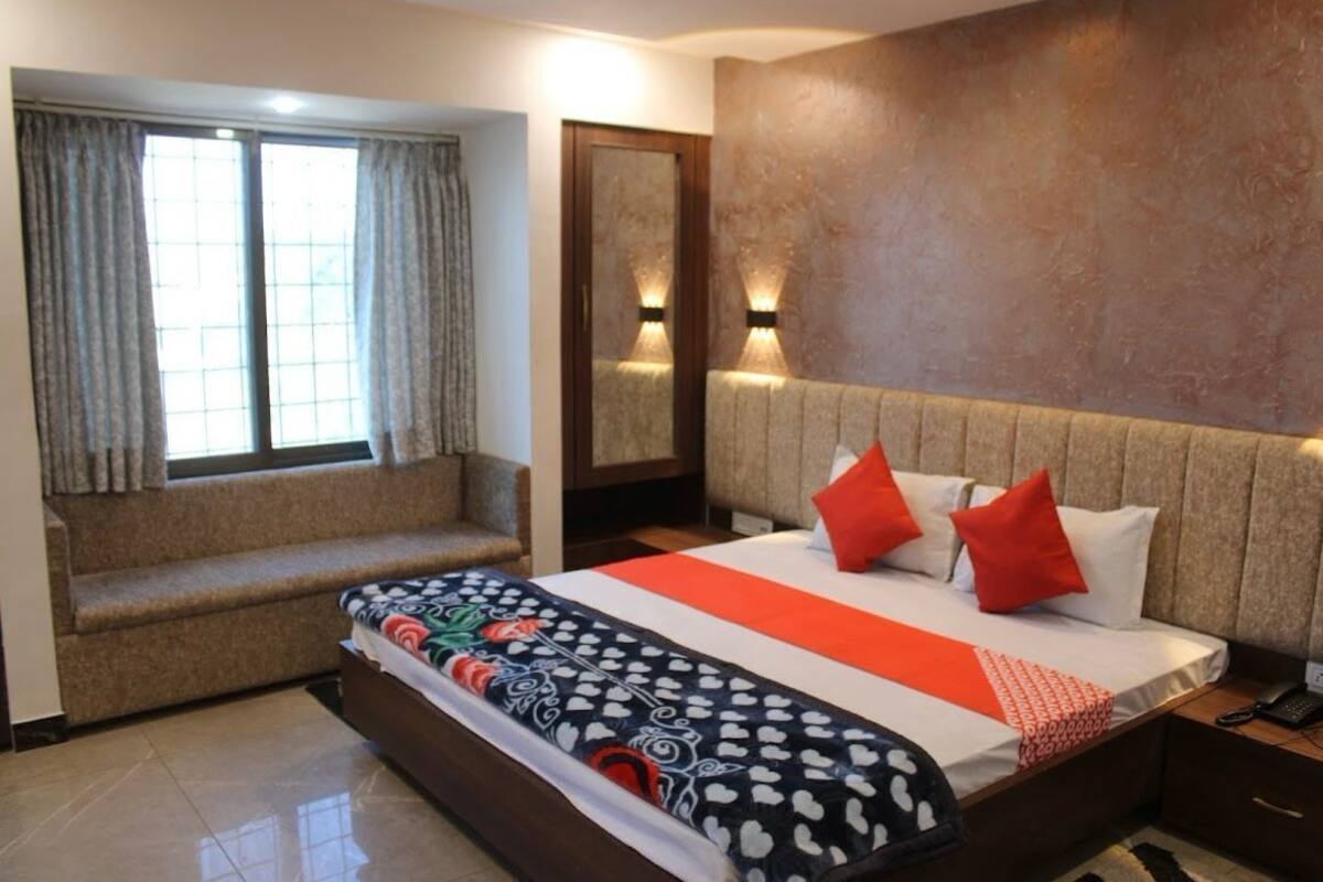Une chambre d’hôtel avec un grand lit, un banc, un miroir et deux lampes fixées au mur.
