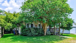 A single-story house with a front porch, surrounded by a well-maintained lawn and various shrubs. - SLW504A: Gone Coastal-Adorable 2 bed, 2 bath Unit Few Blocks from the Beach (Carolina Beach)