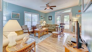 A living room with a ceiling fan, a sofa, a coffee table, a rocking chair, and a television. - SLW504A: Gone Coastal-Adorable 2 bed, 2 bath Unit Few Blocks from the Beach (Carolina Beach)