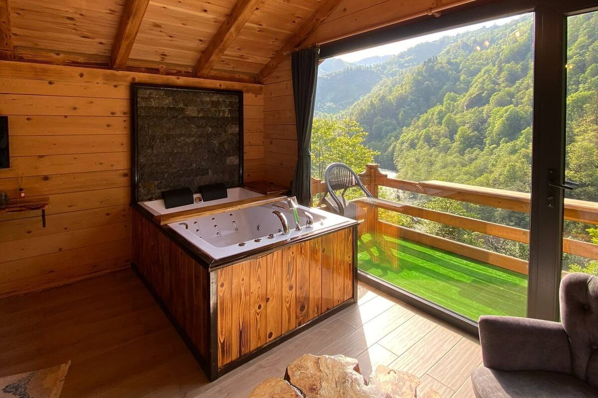 Een houten hut met een hottub, een stenen open haard en een balkon met uitzicht op het bos.